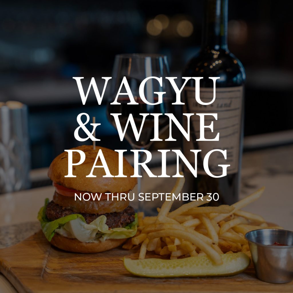 Burger with lettuce and tomato, fries, wine bottle and glass on a wooden board; Wagyu & Wine Pairing now thru September 30 (promo image).